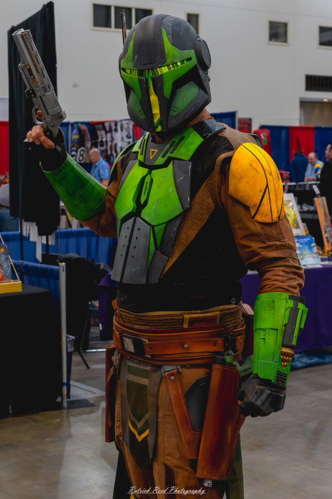 "Cosplayer dressed in green Mandalorian armor, complete with a helmet, chest plate, and matching accessories, embodying the iconic warrior from the Star Wars universe."